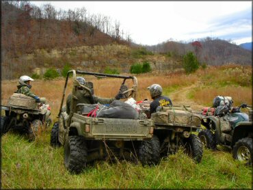 Yamaha Rhino UTV with three Yamaha Grizzly ATVs carrying camping supplies parked off trail.