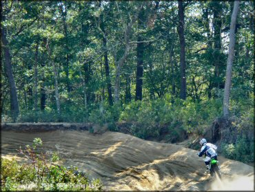 Man riding KX dirt bike through deep sandy whoop section on motocross track.