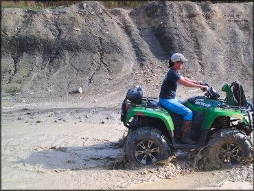 Woman on green Artic Cat ATV going through shallow mud puddle.