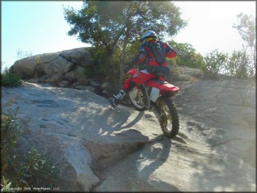 Man wearing red and black Fox motocross gear riding Honda CRF250X navigating short section of solid rock.