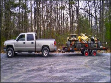 Extended silver cab truck towing a flat bed trailer with three ATVs.