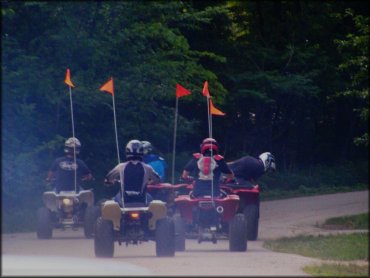 Group of five ATVs with orange whip flags driving to the trails.