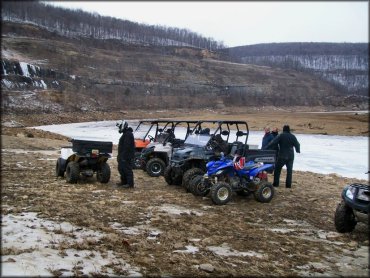 Group photo of three UTVs and three ATVs parked in a line next to a frozen pond.