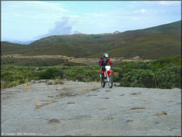 Man on Honda CRF250X riding on solid rock.