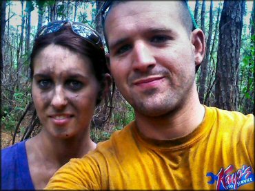 A young woman with muddy face sunglasses propped on top of head standing next to young.