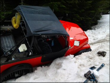 Jeep with a mesh top roof and mud tires stuck in deep snow drift.