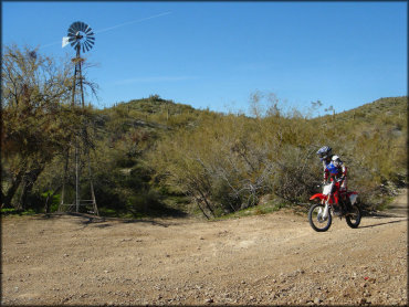 Rider on Honda CRF150R on wide ATV trail going past windmill.
