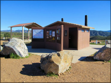 Close up photo of vault toilets, information kiosk, shade gazebo with picnic table surrounded by large boulders.