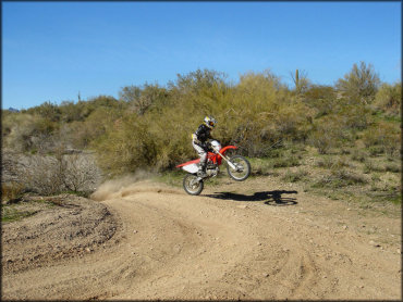 Man on Honda CRF250X dirt bike landing from a small jump.