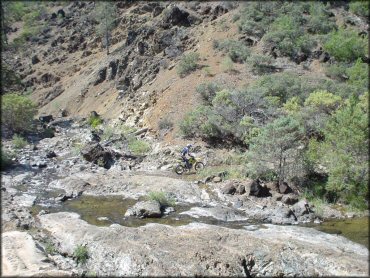 Rider on Suzuki RM 100 dirt bike crossing a shallow stream crossing.