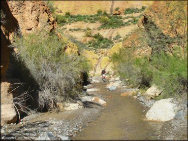 Dirt bike riding through shallow runoff stream.