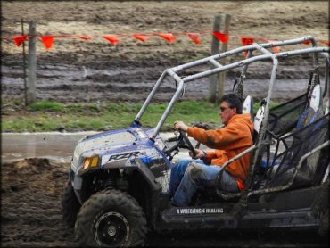 Dark blue Polaris RZR with roll cage going though some mud.