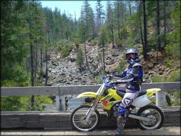 Young woman wearing Acerbis riding gear and Chatterbox radio attached to motorcycle helmet sitting on RM100 dirt bike.