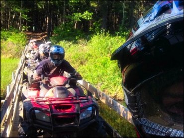 Group of ATV riders riding over a wooden bridge.