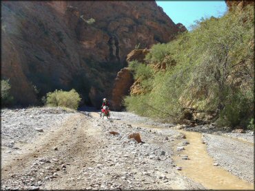 Honda dirt bike going though shallow stream and loose chunk rock.