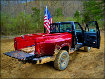 Two toned pickup truck with black cab and red bed parked with American flag in the back.