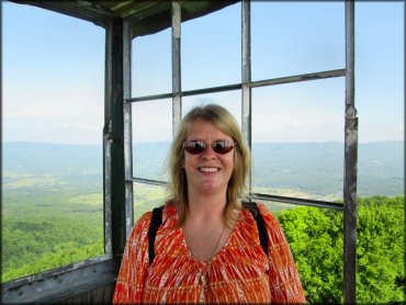 Photo of mature woman with scenic views of valleys, forest and hills taken from top of fire tower.