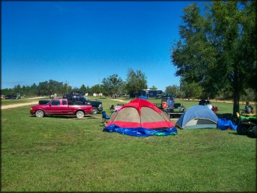 Two tents, ATVs and trucks parked on grassy campsite.