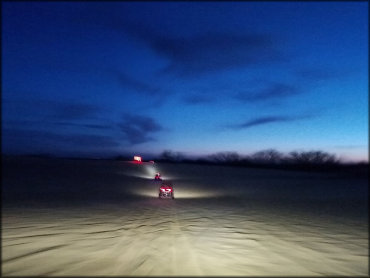 Two UTVs navigating the sand dunes at night time.