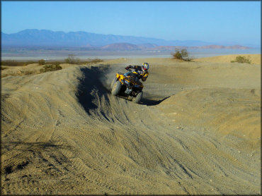 Yellow Honda Fourtrax 250 riding through sandy berm on makeshift motocross track in the desert.