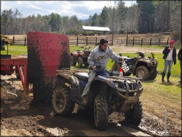 Woman riding blue ATV with mud tires towing a tractor through mud.