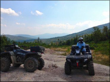 Two Arctic Cat ATVs with mud tires and rear cargo storage boxes.