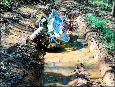 Small white and pink ATV stuck in a deep mud rut.