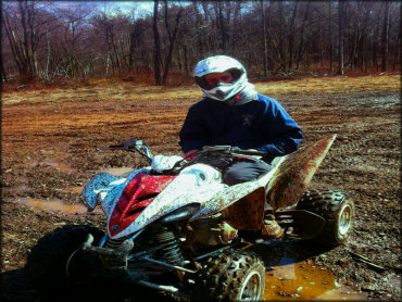 Young man sitting on Yamaha Raptor with red and white plastic covered in mud.