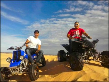 Two men sitting on a blue Yamaha Banshee and black Suzuki ATV.