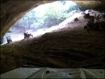 Group of UTVs and ATVs driving through entrance of large cave.