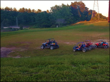 Two side by sides and two go karts in open grassy area.
