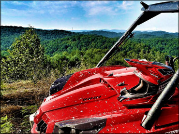 A UTV with a helmet resting on the hood parked on a trail with a scenic backdrop.
