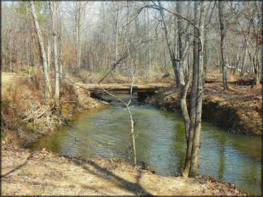 Scenic photo of bridge crossing and shallow creek surrounded by trees.