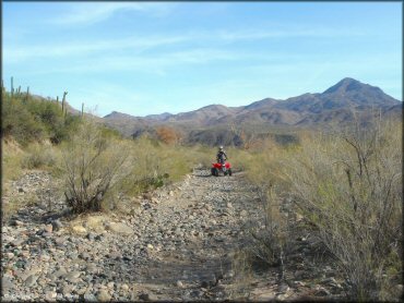 Honda TRX250 navigating trail with loose river rocks.