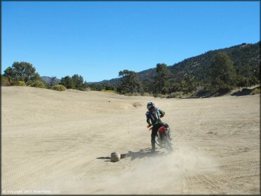 Young woman on Honda CRF150 doing doughnuts in play area.