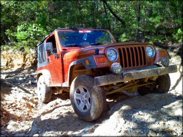 4x4 Jeep with alloy rims and PIAA lights climbing a rocky section of trail.