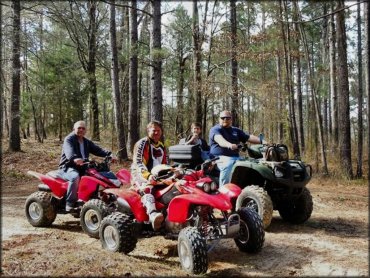 Group photo of three men and one small child each sitting on a four wheeler.