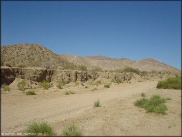 A scenic portion of a hard packed desert trail surrounded by barren rolling hills.
