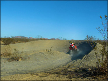 Woman on Honda TRX 250 riding through deep berm on make-shift motocross track in the desert.