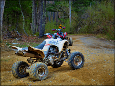 Two Yamaha ATV Raptors parked next to trail with signage in the back.
