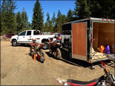 Box trailer with white pickup truck and four dirt bikes at staging area.