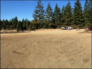 Two men with three Honda dirt bikes and other trucks parked in staging area.