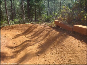 Section of reddish colored ATV trail with wooden guard rails on berm.