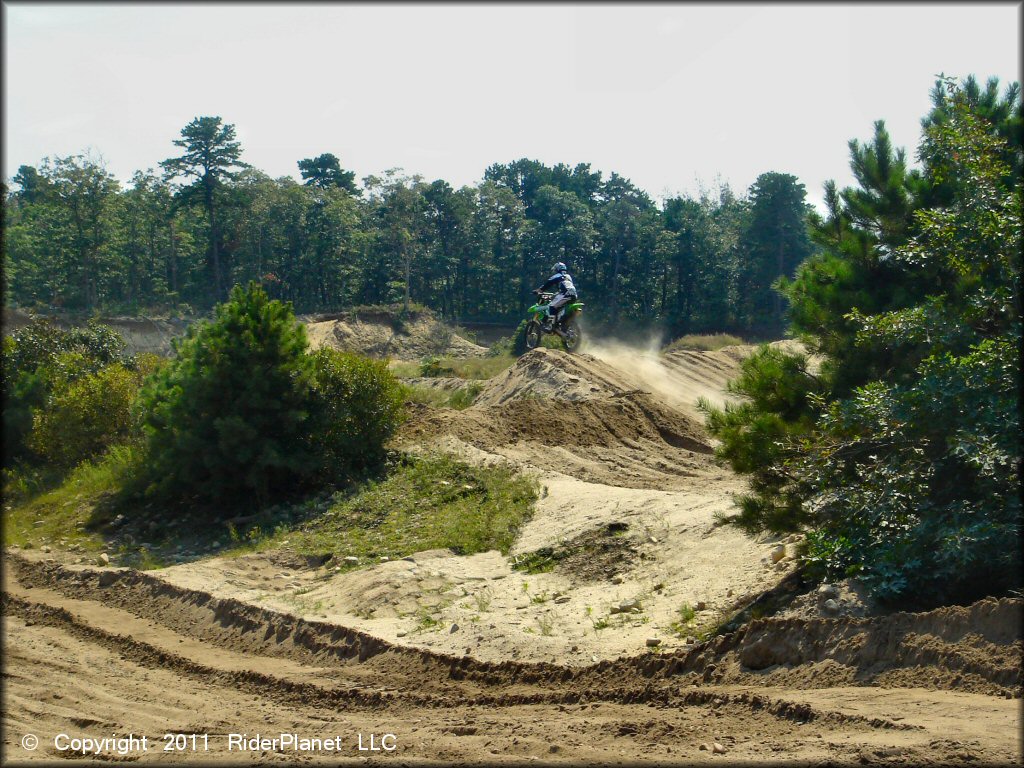 Kawasaki four-stroke going over jump on motocross track.