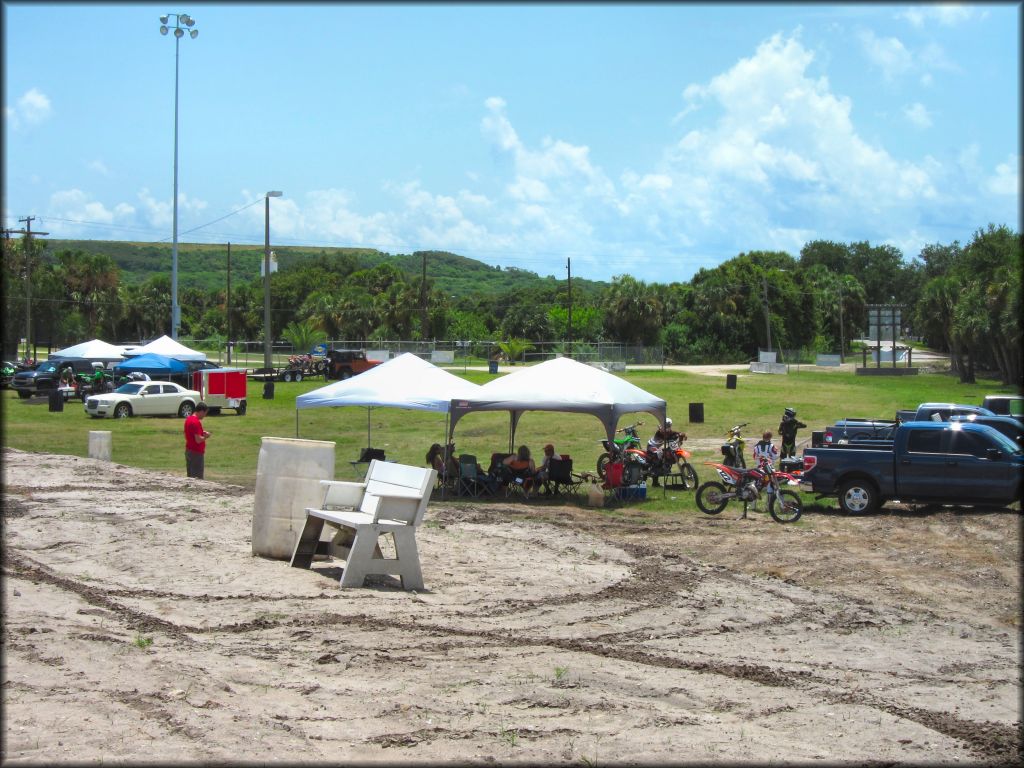 Grassy staging area with several trucks, cars and pop up tents and trash cans.