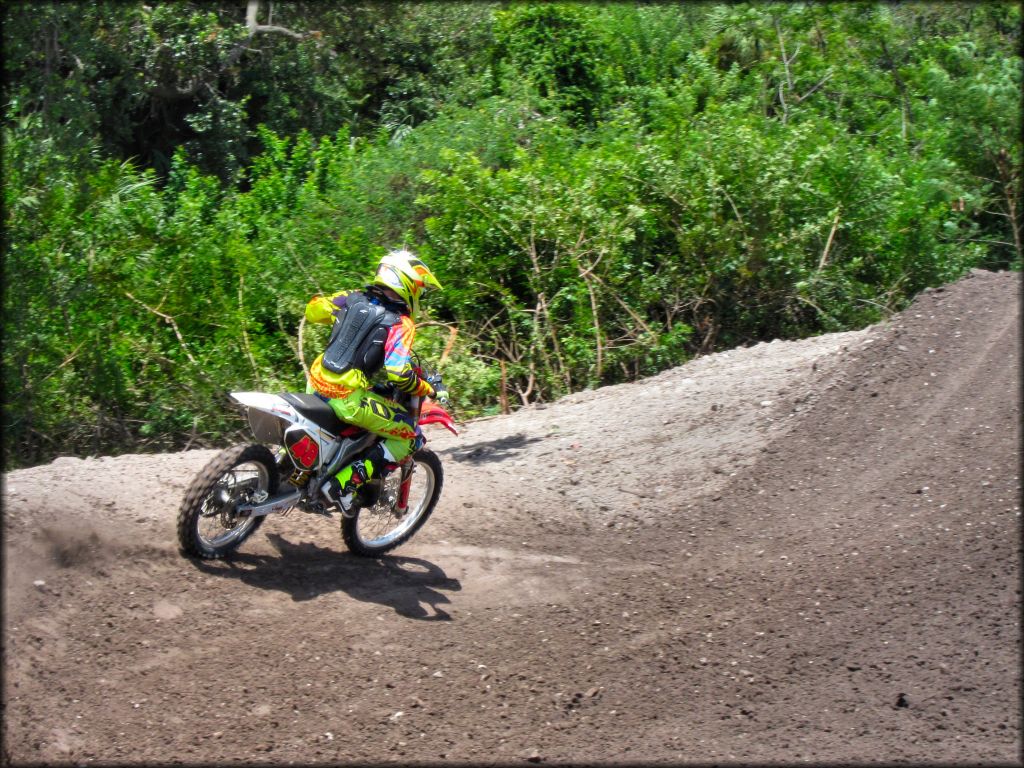 Man wearing Fox Racing motocross gear on Honda dirt bike heading up jump on motocross track.