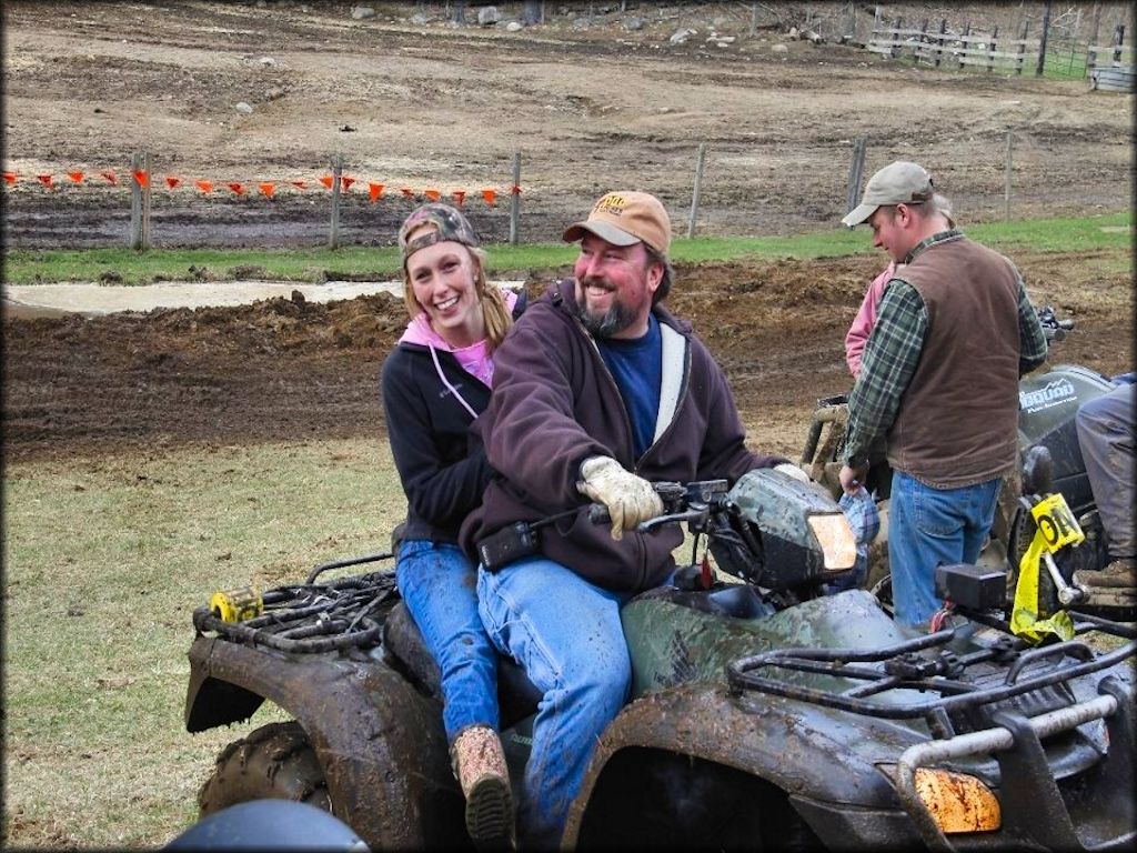 Man and woman sitting on a dark green Honda ATV.