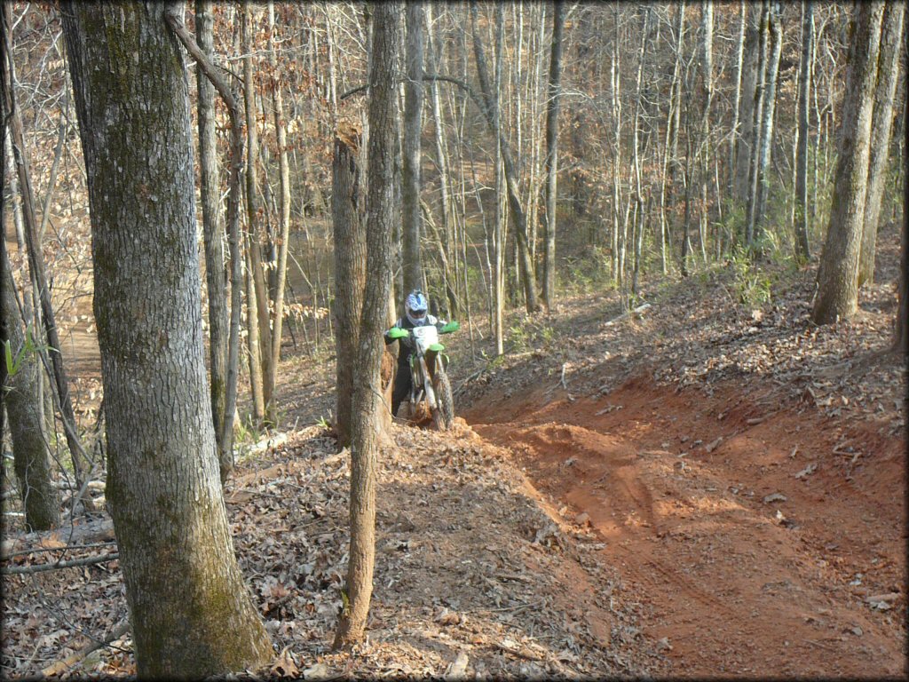 Man on Kawasaki dirt bike trying to go up steep and rutted ATV trail.