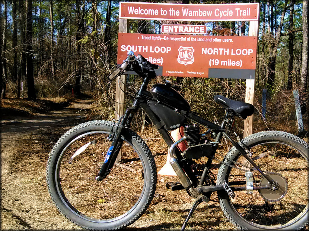 A motorized bicycle parked near the trail entrance.