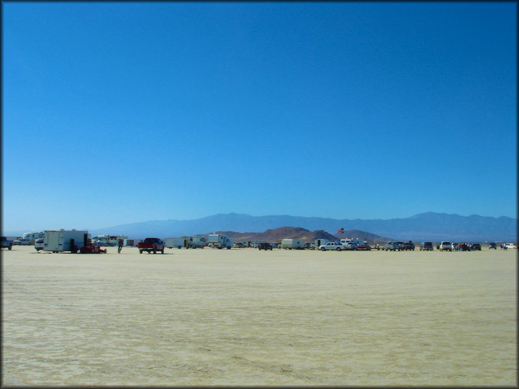A large group of RV campers and trucks parked on a dry lake bed.
